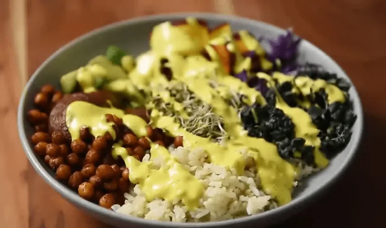 "Close-up of a healthy, vibrant Buddha bowl containing rice, various vegetables, beans, and sprouts, all covered in a bright yellow, creamy dressing.