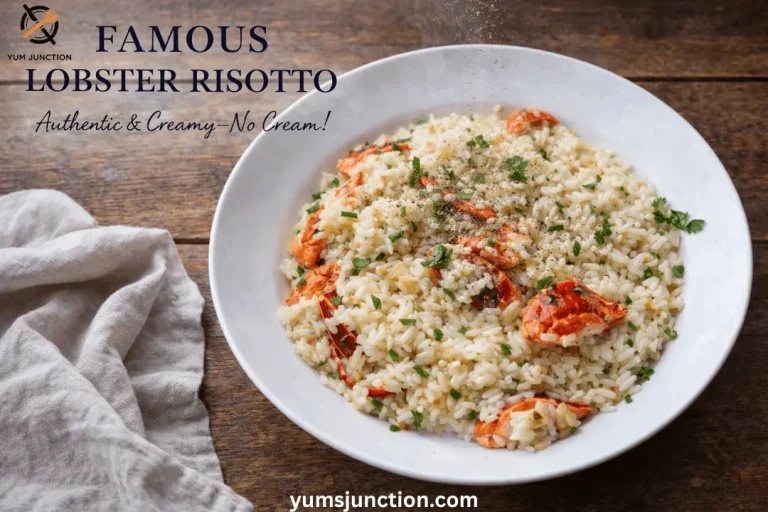 A horizontal food graphic titled "FAMOUS LOBSTER RISOTTO" with the subtitle "Authentic & Creamy—No Cream!" The image shows a white bowl of lobster risotto on a rustic wooden table next to a grey linen napkin. A fine dusting of black pepper is being sprinkled over the dish. The website "yumsjunction.com" is printed at the bottom.