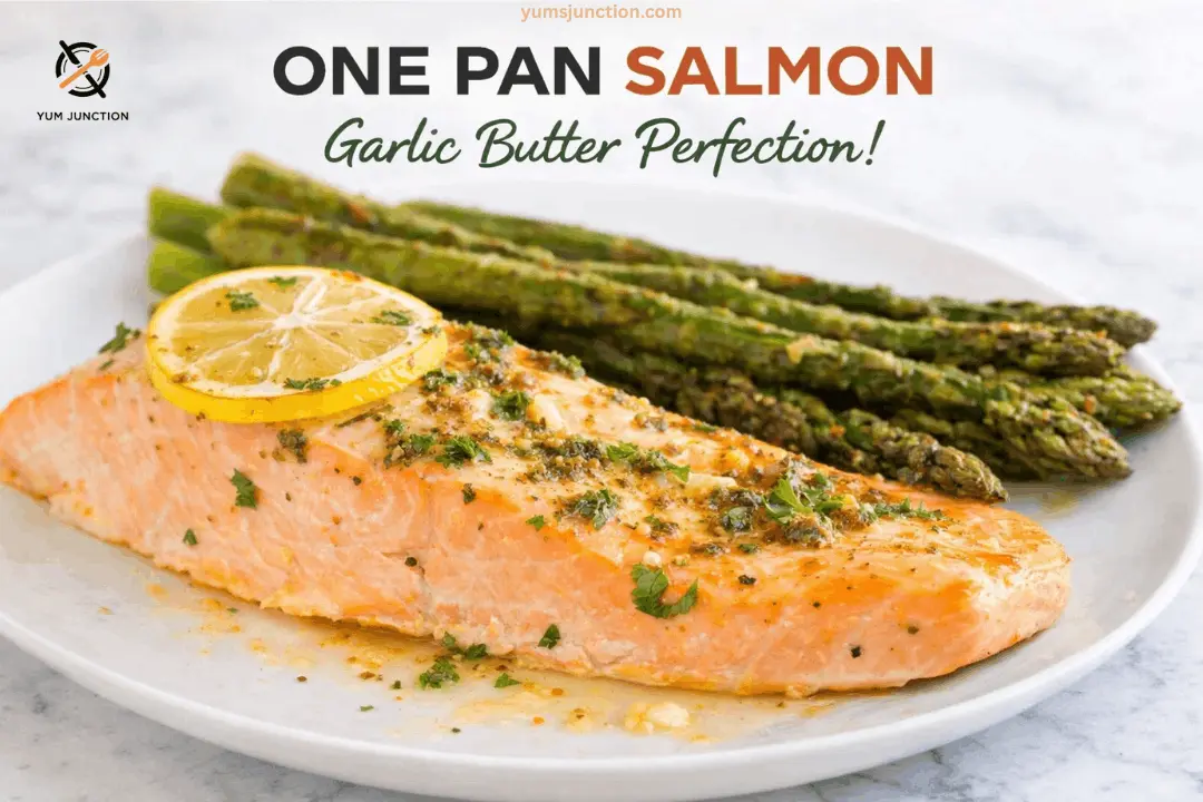 A professional food graphic for "ONE PAN SALMON Garlic Butter Perfection!" featuring a large, flaky salmon fillet drizzled with a rich garlic herb butter sauce. A fresh lemon slice sits on top, and several spears of roasted asparagus are on the side. The dish is presented on a white plate against a light grey marble background. The Yum Junction logo and website address are at the top.