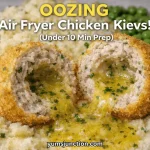 Promotional food graphic titled "OOZING Air Fryer Chicken Kievs!" with "Under 10 Min Prep" in text. The image is an extreme close-up of a breaded chicken ball split in two, with a stream of hot, melted yellow herb butter pouring out onto a bed of mashed potatoes. The Yum Junction logo and website URL are clearly visible.