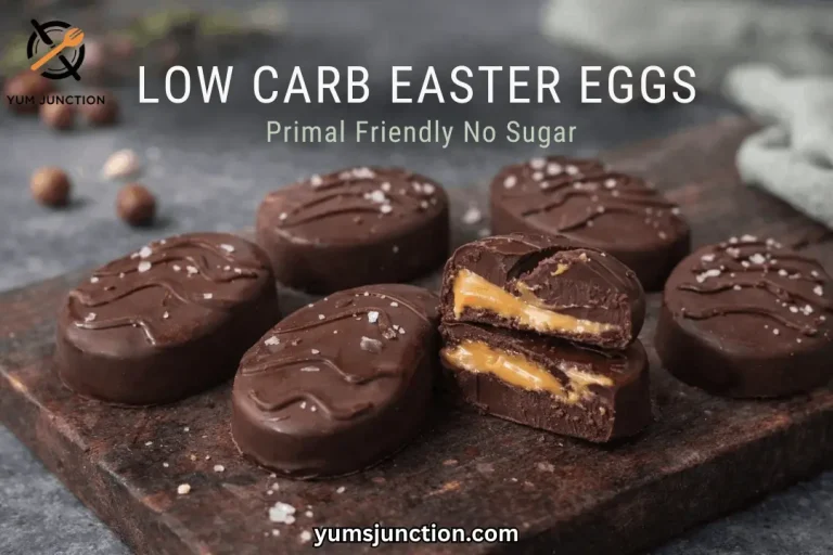 A horizontal promotional graphic for Yum Junction. Large white text at the top reads "LOW CARB EASTER EGGS," with the subtitle "Primal Friendly No Sugar" below it. The image displays a group of dark chocolate-covered egg treats on a dark, rustic wooden cutting board against a moody grey background. A halved egg in the foreground shows a gooey, caramel-style center. All eggs are topped with decorative chocolate lines and large sea salt crystals. The Yum Junction logo is in the top left, and the URL "yumsjunction.com" is at the bottom center.