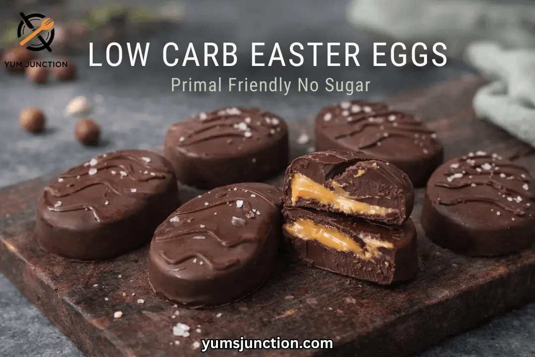 A horizontal promotional graphic for Yum Junction. Large white text at the top reads "LOW CARB EASTER EGGS," with the subtitle "Primal Friendly No Sugar" below it. The image displays a group of dark chocolate-covered egg treats on a dark, rustic wooden cutting board against a moody grey background. A halved egg in the foreground shows a gooey, caramel-style center. All eggs are topped with decorative chocolate lines and large sea salt crystals. The Yum Junction logo is in the top left, and the URL "yumsjunction.com" is at the bottom center.