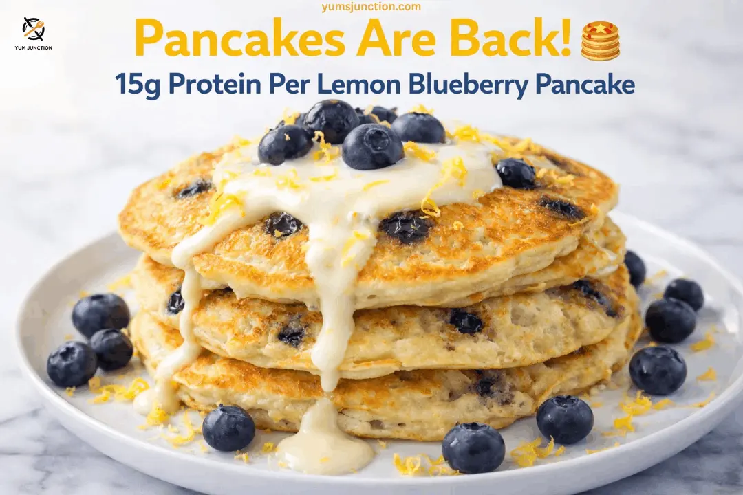 A professional food graphic for Yum Junction featuring a stack of three thick, golden-brown pancakes filled with blueberries. The pancakes are topped with a thick, creamy white glaze that drips down the sides, along with fresh blueberries and yellow lemon zest. The scene is set on a white marble surface with scattered blueberries. Text at the top reads "Pancakes Are Back! 15g Protein Per Lemon Blueberry Pancake" with the website yumsjunction.com included.