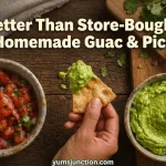 from Yum Junction a horizontal promotional graphic with the text "Better Than Store-Bought! Homemade Guac & Pico." The image shows a hand dipping a tortilla chip into a bowl of bright green guacamole next to a bowl of fresh pico de gallo, surrounded by fresh cilantro and lime.