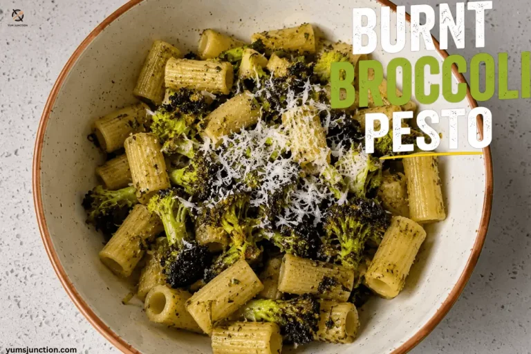 A top-down view of a bowl filled with rigatoni pasta tossed in vibrant green pesto, topped with charred burnt broccoli florets and freshly grated parmesan cheese, labeled with the text "Burnt Broccoli Pesto"