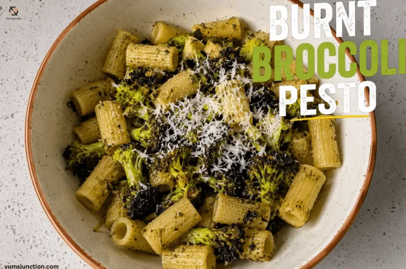 A top-down view of a bowl filled with rigatoni pasta tossed in vibrant green pesto, topped with charred burnt broccoli florets and freshly grated parmesan cheese, labeled with the text "Burnt Broccoli Pesto"