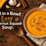 Bowl of butternut squash soup surrounded by raw squash, garlic, and cinnamon sticks on a wood table
